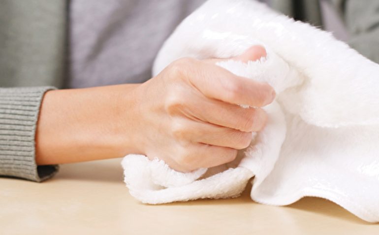 Eine Person sitzt an einem Tisch und hält ein weißes, flauschiges Handtuch in ihren Händen. Es sieht aus, als würde sie das Handtuch benutzen, um Schweiß von ihren Händen abzuwischen, was auf Probleme mit übermäßigem Schwitzen hinweisen könnte.