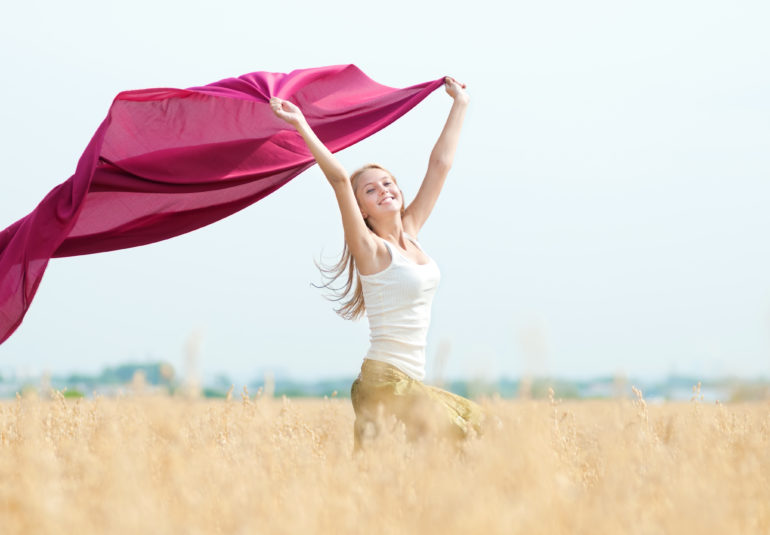 Eine Frau auf einem Feld, die einen rosa Schal in der Hand hält, erlebt Linderung ihrer Menstruationsschmerzen.