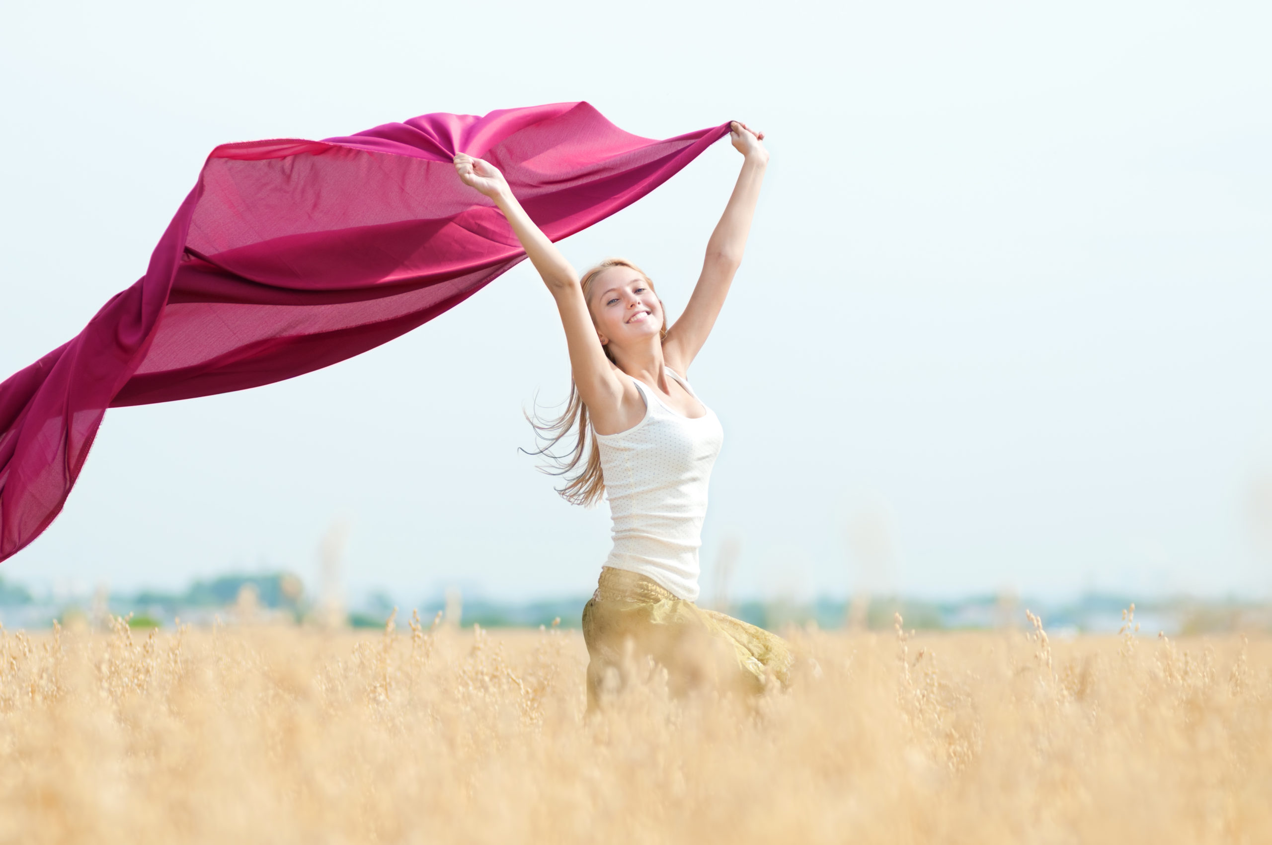 Eine Frau auf einem Feld, die einen rosa Schal in der Hand hält, erlebt Linderung ihrer Menstruationsschmerzen.