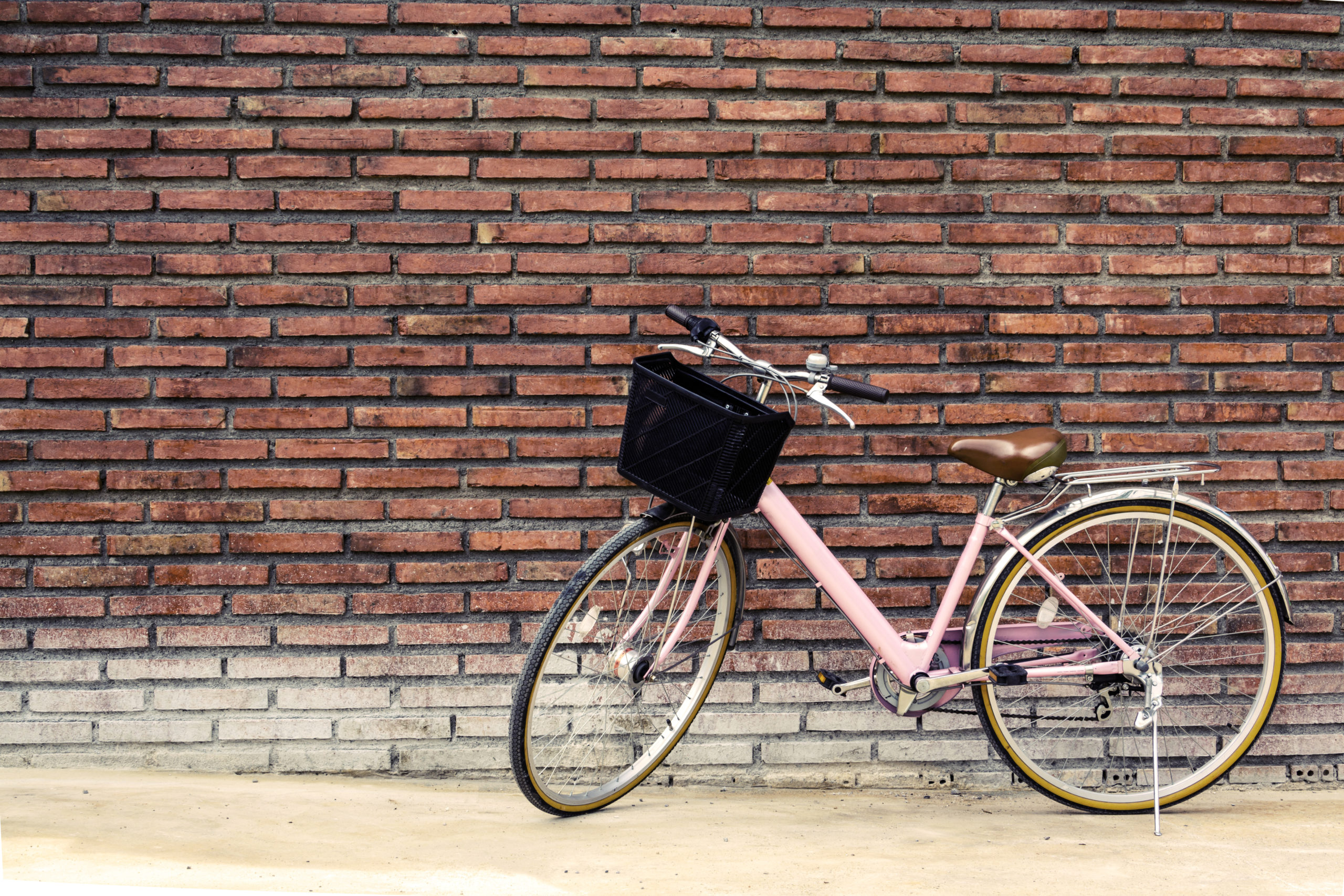 Ein rosafarbenes Fahrrad, das an einer Ziegelwand lehnt.
