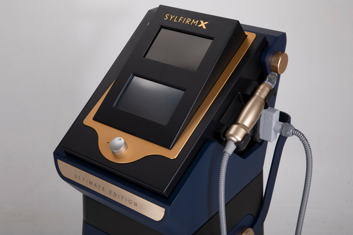 Moderne medizinische Ausrüstung namens SYLFIRM X, Ultimate Edition, in Marineblau und Gold. Das Gerät verfügt über ein großes Touchscreen-Display, Einstellknöpfe und angeschlossene Handstücke mit Kabeln.